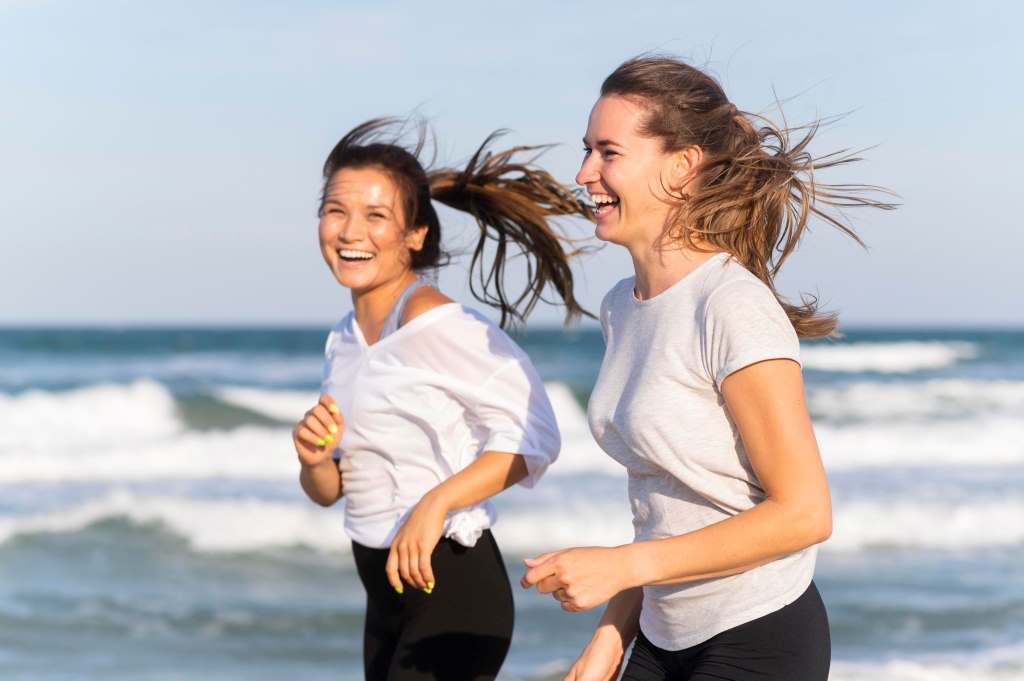 smiley women running together on the beach